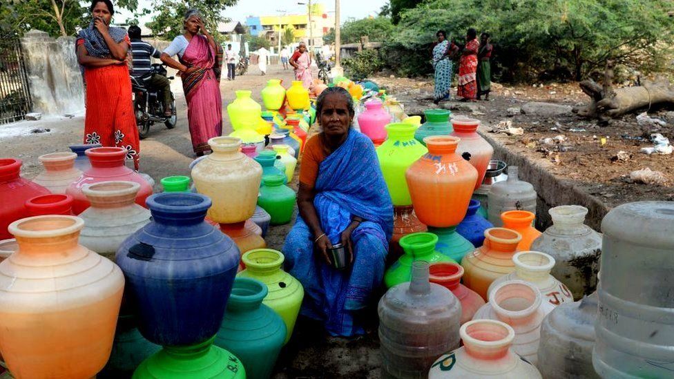 A woman sits amid empty water pots