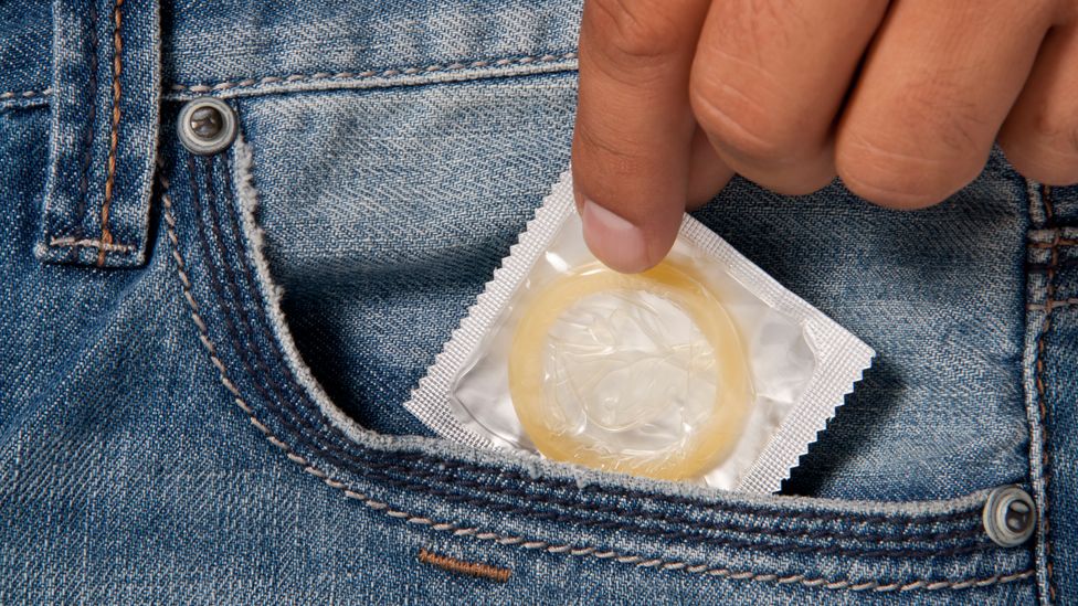 A person pulling a condom out of their pocket