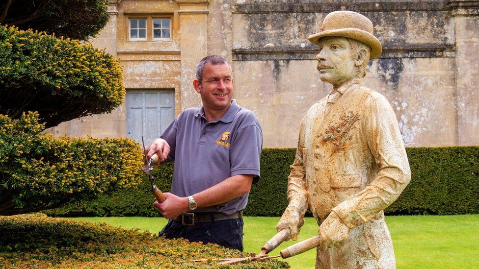 Longleat's head gardener standing next to a statue of his predecessor from 1902