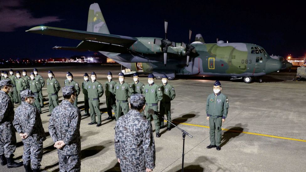 Japanese military officers stand in ceremony in front of a C-130 Hercules carrying relief supplies to be deployed to Tonga