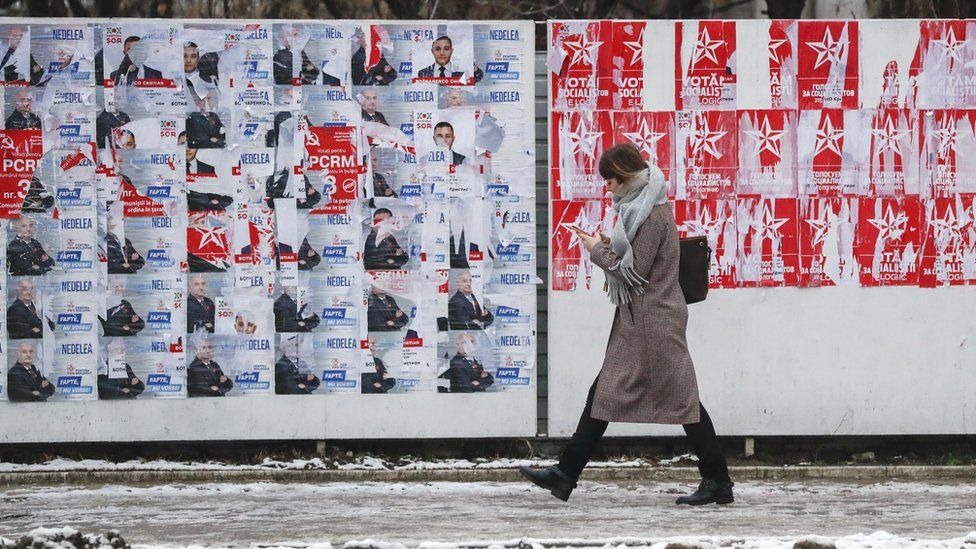 A woman walks past a wall with, on one side, the blue posters of the country's democratic party, and one the left, the red posters of the socialists