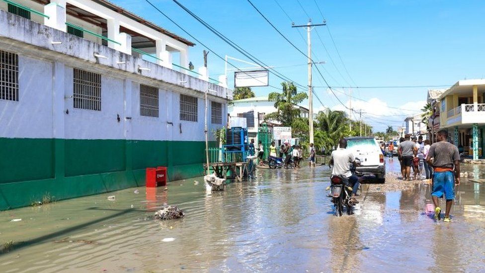 Groups of people walk through a flooded street in Les Cayes
