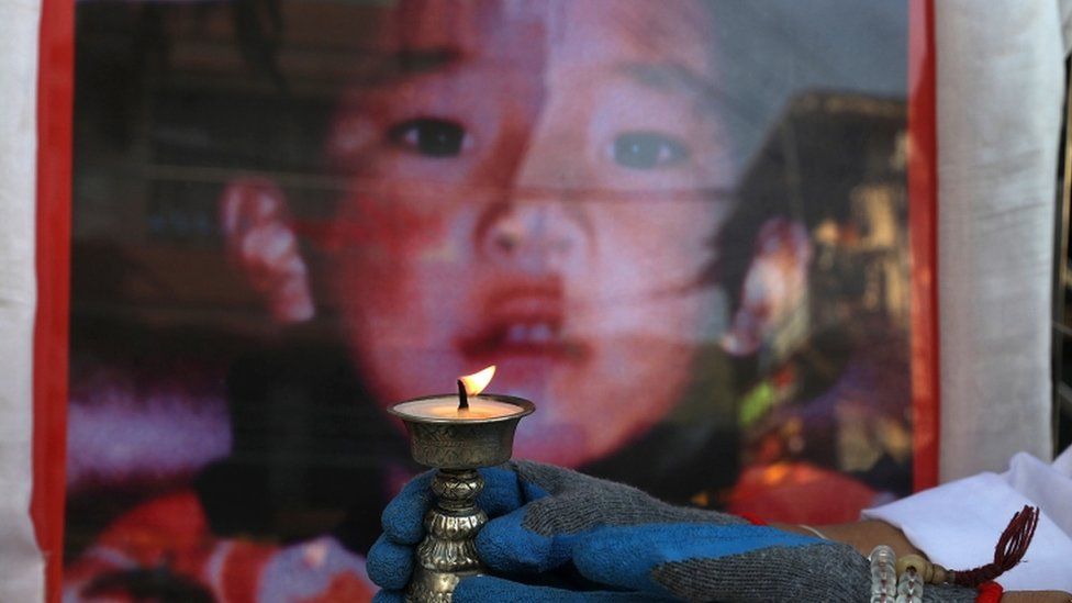 A woman holds a candle in front of a picture of the Panchen Lama to mark his 31st birthday in 2020