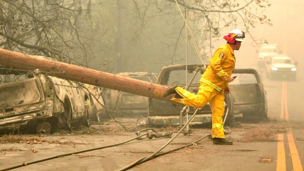A firefighter steps over a downed power line as he surveys abandoned burned cars on the side of the road after the Camp fire tore through the area in Paradise, California, 10 November 2018