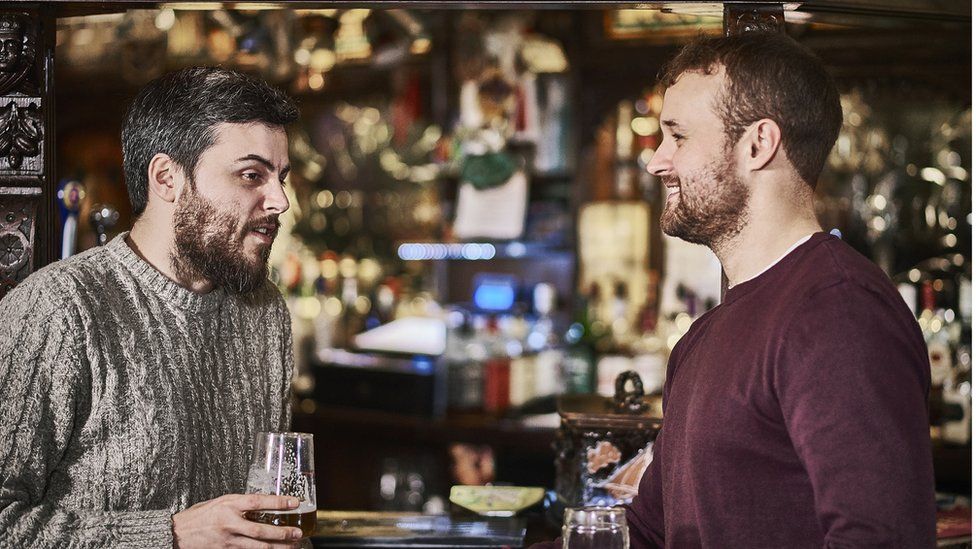 Two male bearded friends stood at the bar
