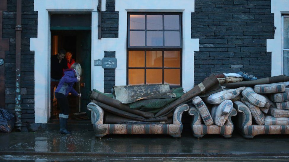 Woman sweeps water out of house with furniture abandoned outside