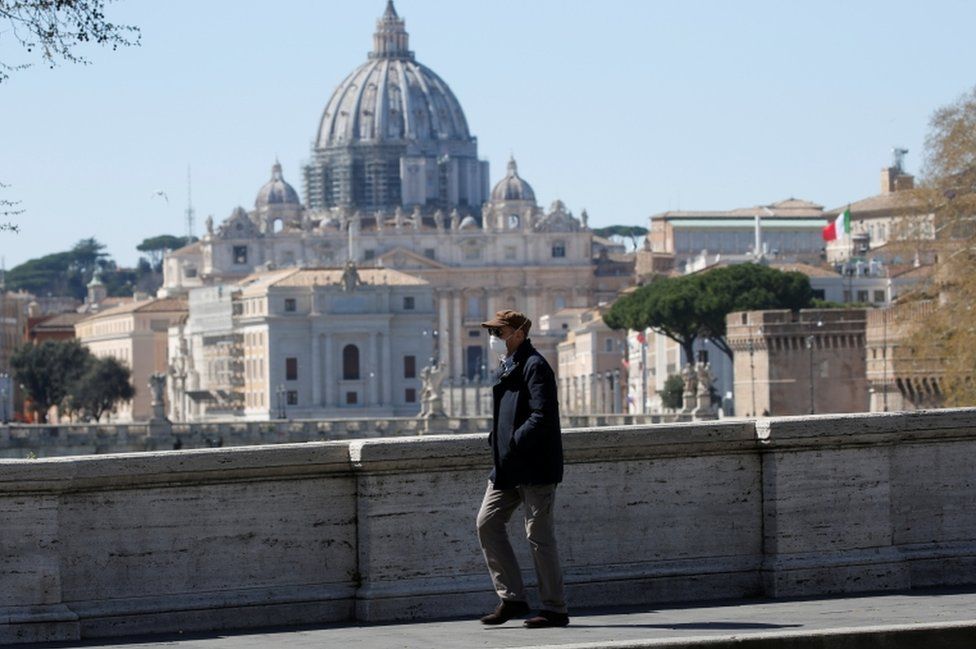 A man wearing a face mask walking past St Peter's Basilica