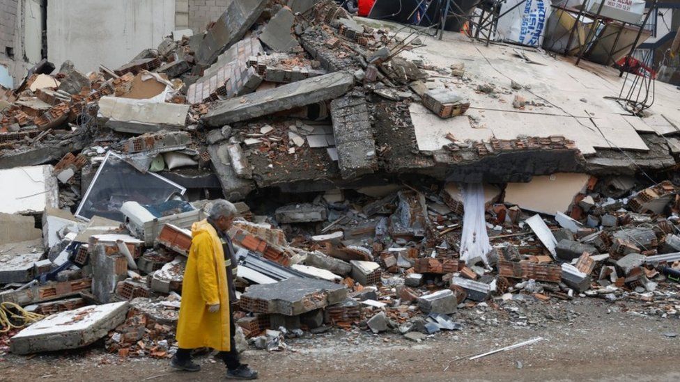 A man stands in front of a collapsed building, following an earthquake in Kirikhan, Hatay, Turkey