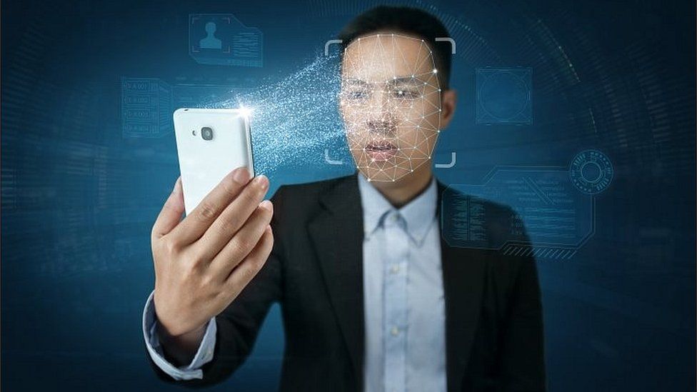 Young modern man in suit holds up a smartphone to his face, enabling facial recognition