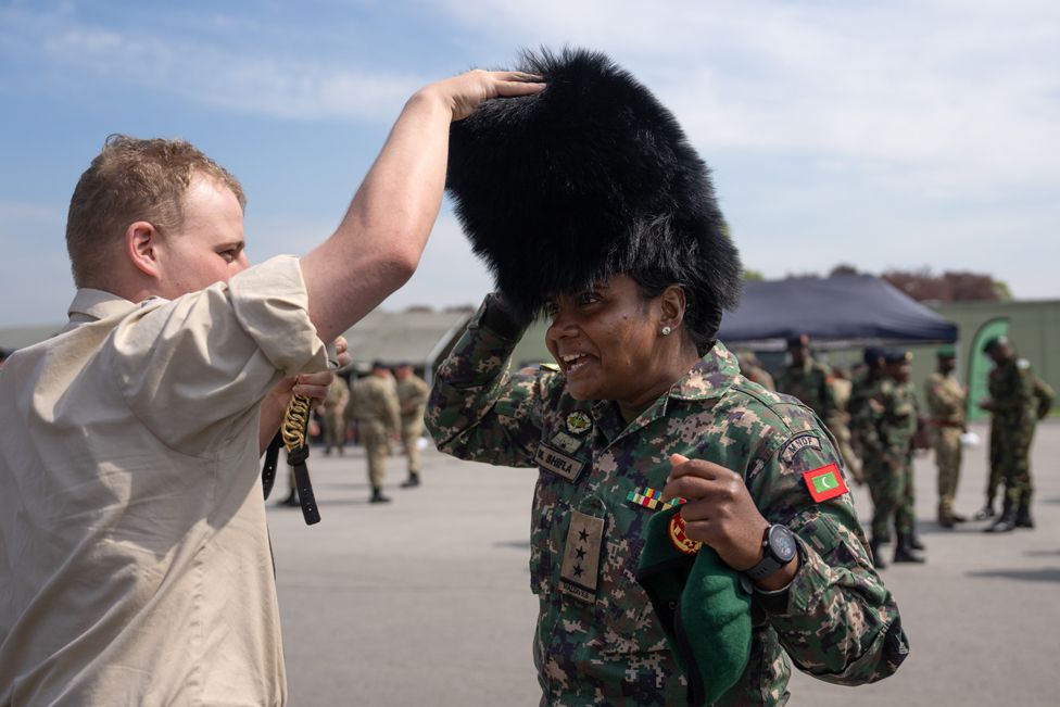 A captain in the Maldives National Defence Force tries on a bearskin hat belonging to a British Guardsman after a military parade for representatives of the Commonwealth taking part in the Coronation, at Army Training Centre Pirbright.