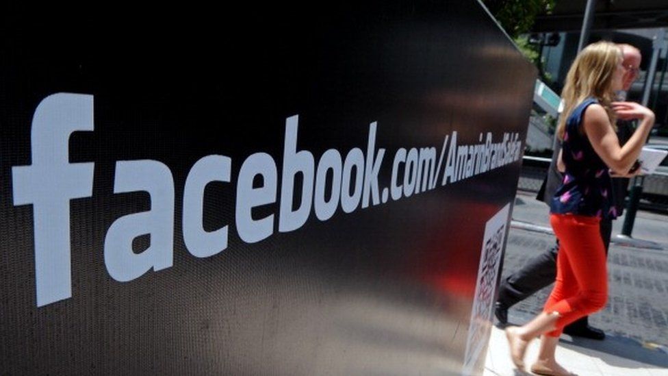 Foreign tourists walk past a Facebook logo displayed at shopping mall in Bangkok on May 15, 2012.