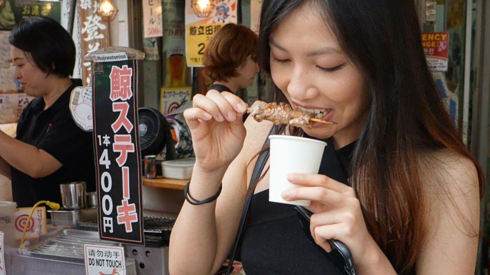 A woman eating whale meat in front of Tokyo's whale meat restaurants