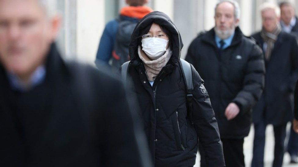 People walking in Holborn, London , one wearing a mask.