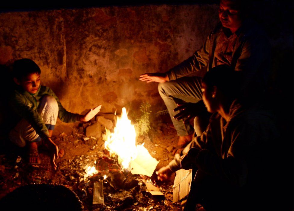 Three people hold their hands up to a campfire for warmth
