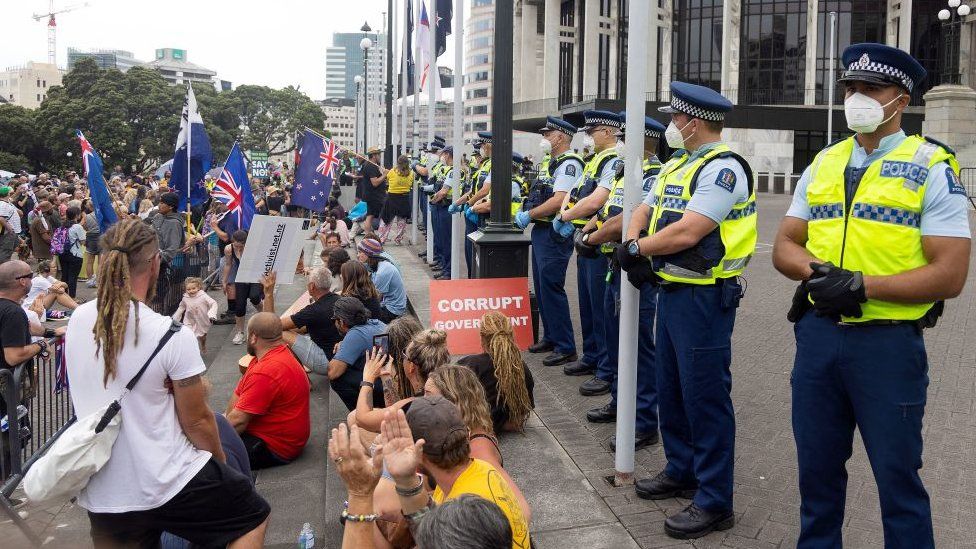 Police (R) watch as protesters occupy the grounds around the parliament building in Wellington on February 9, 2022,