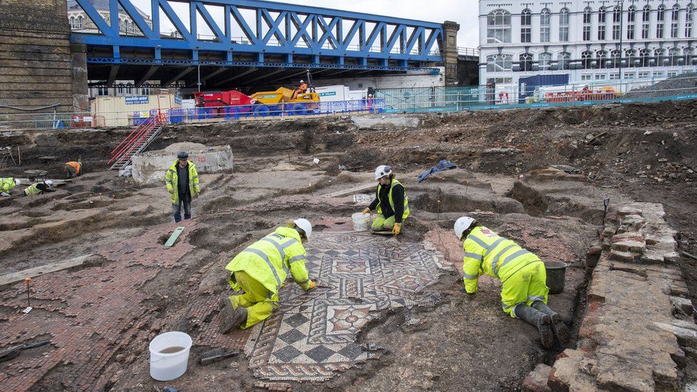 Archaeologists uncover the mosaic while a train bridge is in the background