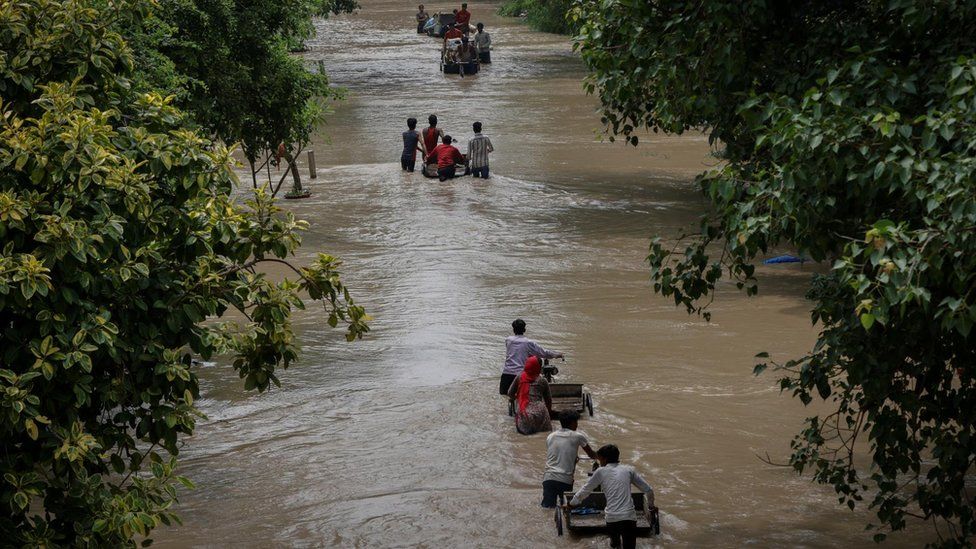 Residents carry their belongings along a flooded street in Delhi