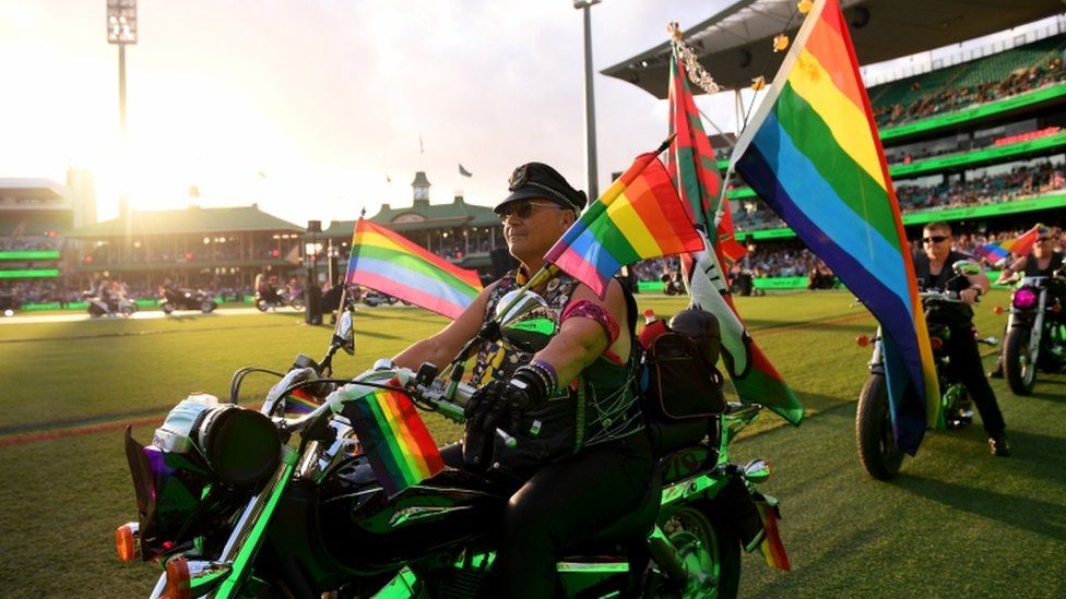 Someone is seen on a motorbike with lots of rainbow flags