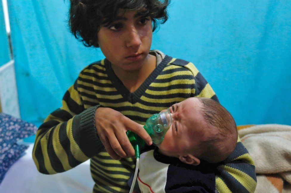 A Syrian boy holds an oxygen mask over the face of an infant at a make-shift hospital following a reported gas attack on the rebel-held besieged town of Douma in the eastern Ghouta region on the outskirts of the capital Damascus on January 22, 2018