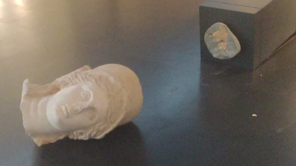 Head of a statue lies on the floor, next to the plinth it has been knocked off of