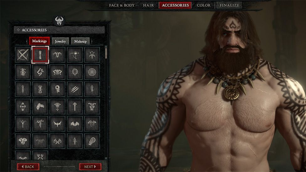 Diablo IV's character creator screen shows a muscular warrior character on the right of the screen. He has ornate, matching tattoos on both arms. He has a mean look, which is emphasised by his long dark hair which covers his bearded face. He wears a circular gold medallion which has teeth or bones at either side of it. A range of character creation options - Face & Body, Hair, Accessories, Color and Finalize - are visible at the top of the screen. To the left, the Accessories window can be seen, showing a range of options for Markings, Jewelry and Makeup. Back and Next buttons are visible at the bottom of the window.