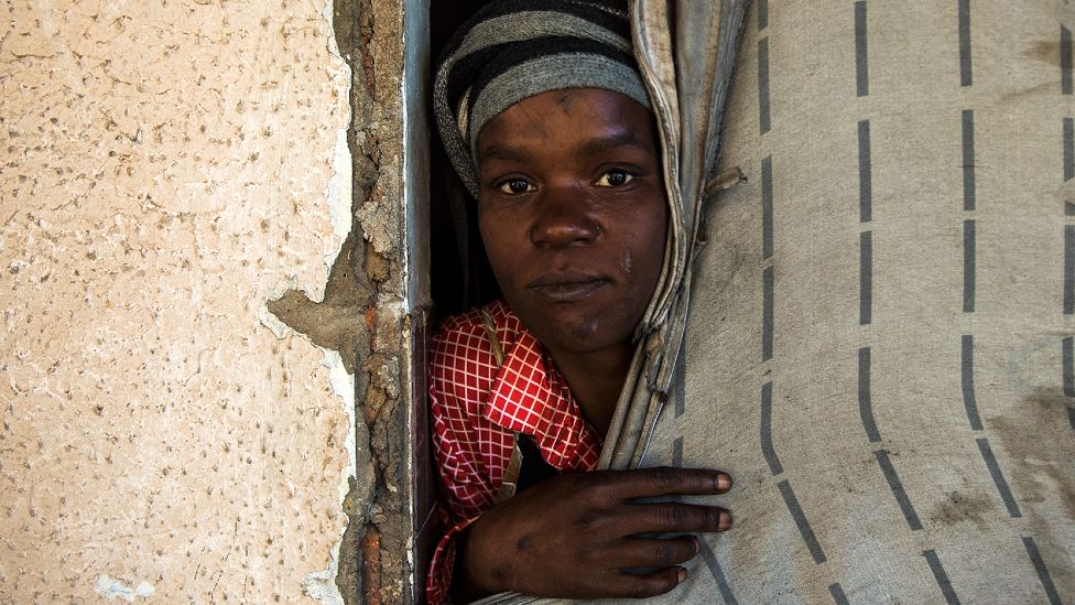 An unidentified woman peeks out of her room. With the doors and door frames removed, a fabric sheet serves as a makeshift door in the derelict San Jose building in Johannesburg, South Africa