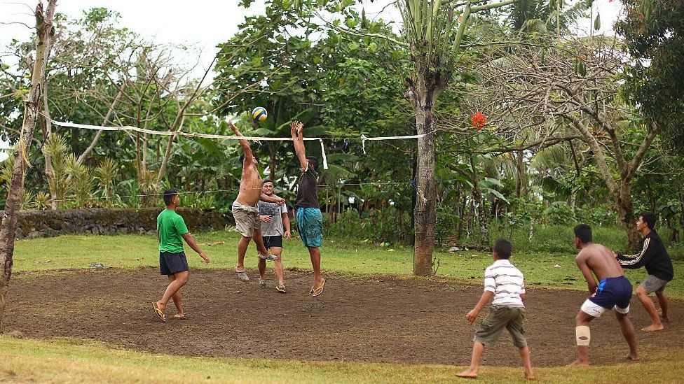 A group of local men and boys play volleyball on a road side court in their village outside of Lotofaga