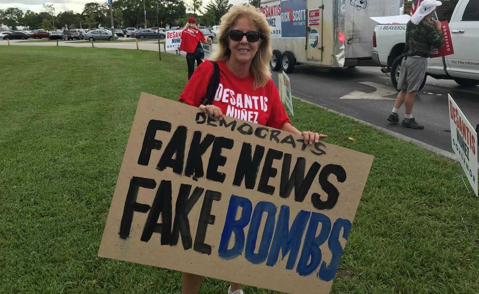 A Republican outside the Florida governor debates on Wednesday holds a sign accusing Democrats of "fake bombs"