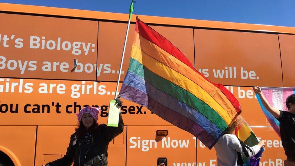 a woman holds a pride flag with a mop as a handle