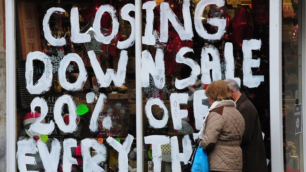 People walk past a store with the words 'Closing down sale 20% off everything' painted on the window