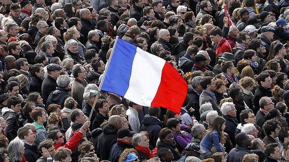 A man holds a French national flag in the middle of a large crowd