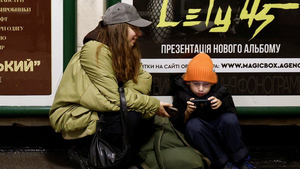 Женщина с маленьким ребенком сидят на станции метро, ​​чтобы укрыться во время воздушного налета в Киеве