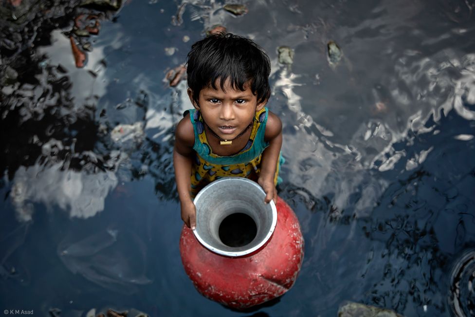 A young girl looks up as she collects water: