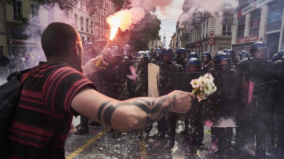 A protester faces police with a torch and a bouquet of flowers in Lyon, 26 May