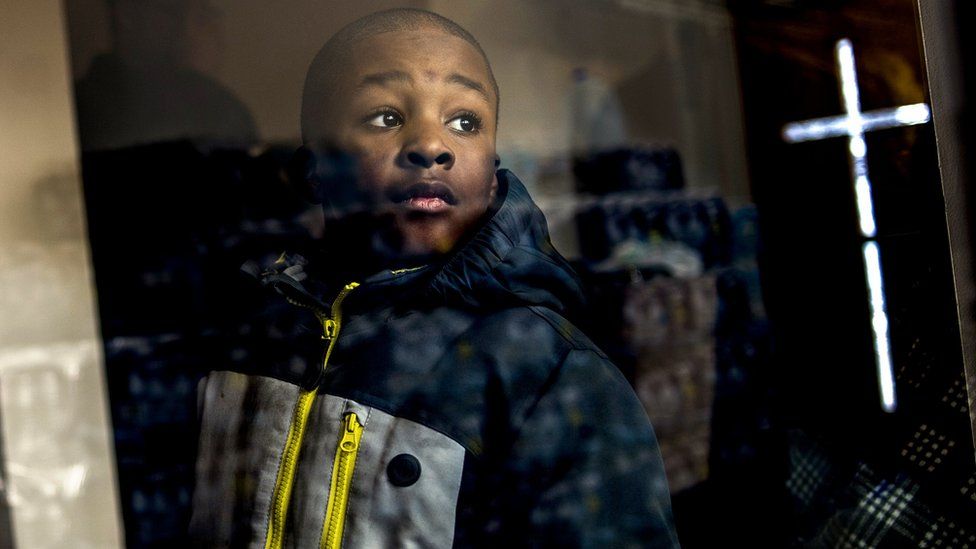 Boy looks at stacks of water in Flint