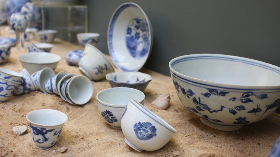 Pieces of blue and white porcelain sitting in sand in a display cabinet