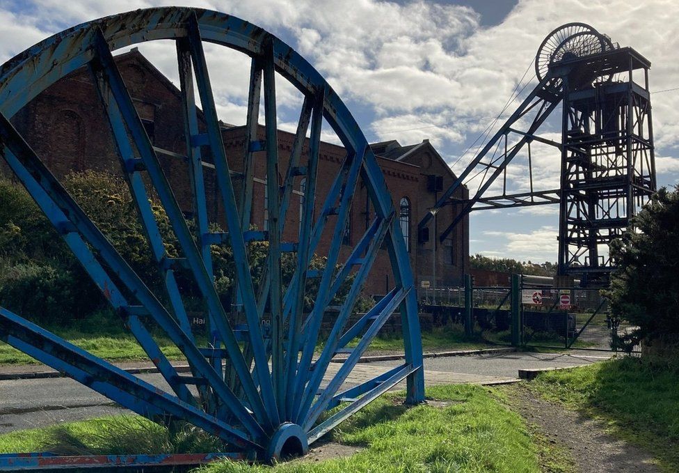 A large blue mine wheel next to a big building