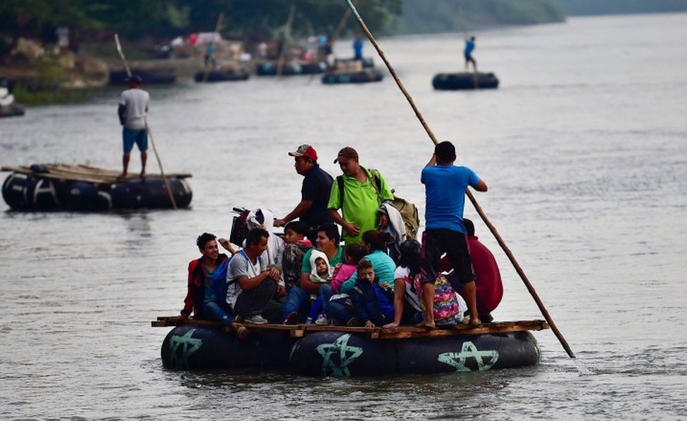 Several makeshift rafts carry migrants across the river