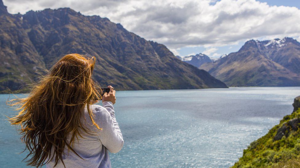 Stock image of a woman photographing mountains and lake, Queenstown, Otago, New Zealand