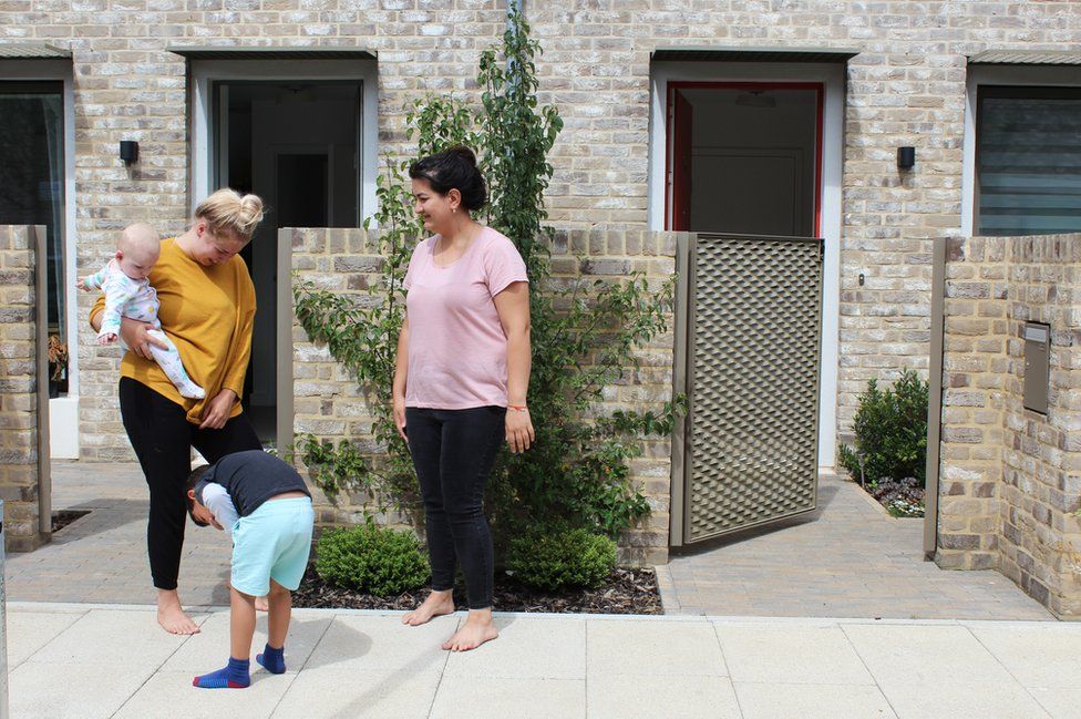 Two mothers and their children stand outside their houses