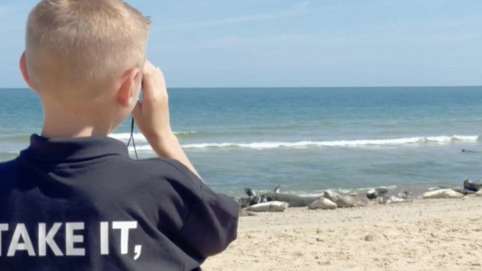 Theo looks through binoculars to see the seals on the beach