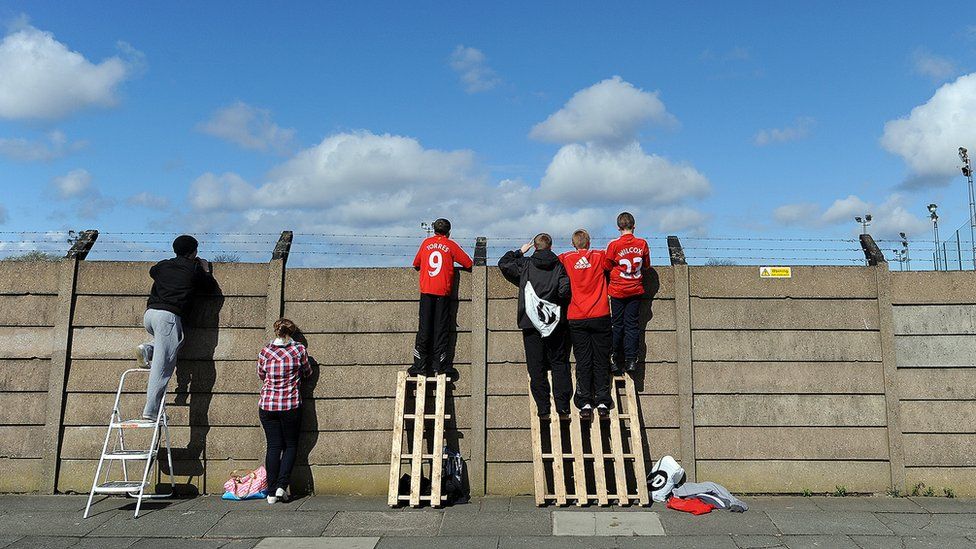 Youngsters climb onto a wall in order to see the Liverpool football squad training at Melwood on April 7, 2009, ahead of their UEFA Champions League quarter final first leg football match against Chelsea on April 8