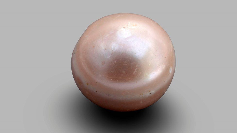 The pearl is round, shiny and appears light pink in color