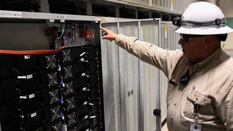 A worker pointing to batteries at an energy storage facility in California