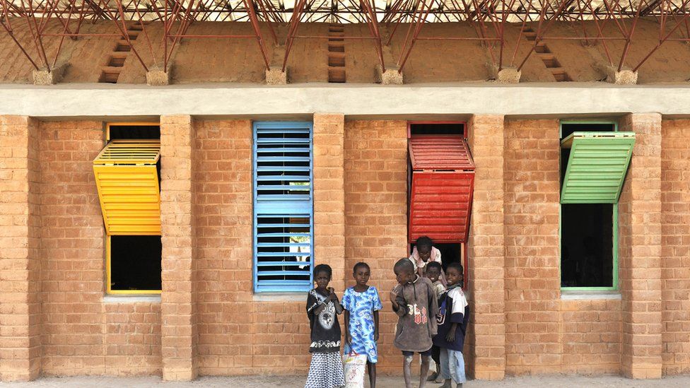 Gandp Primary School. There are 6 children in the photo. There are colourful shutters behind them.