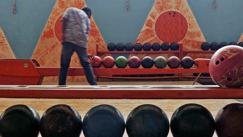 man taking bowling ball from queue in an art deco bowling alley