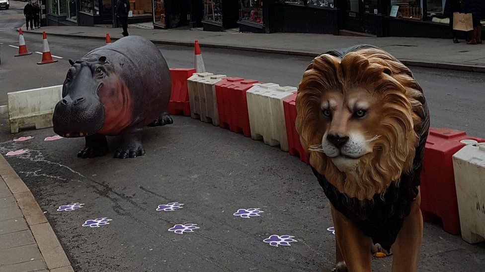 A fibre glass hippo and lion on the road