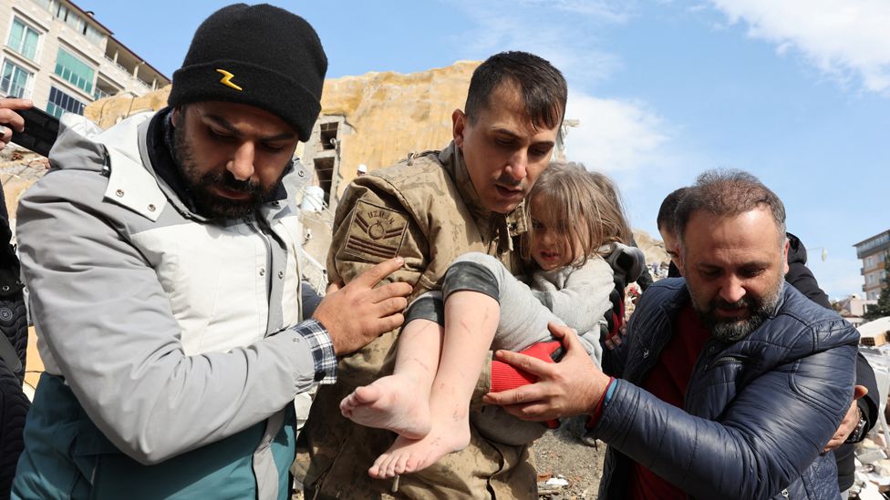 A child is carried out by rescuers from the site of a damaged building, following an earthquake in Hatay, Turkey, on 7 February 2023