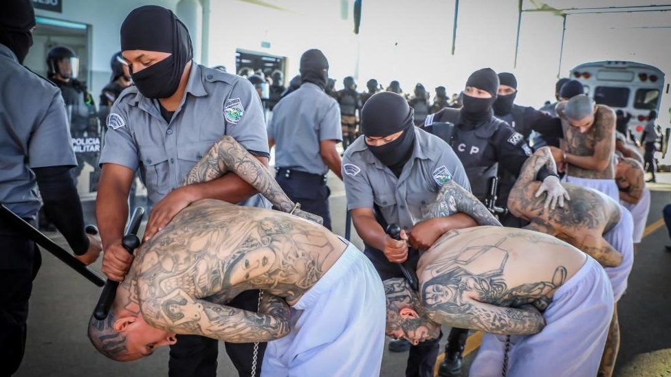 Los agentes penitenciarios custodian a los pandilleros mientras son procesados ​​a su llegada después de que 2000 pandilleros fueran trasladados al Centro de Confinamiento contra el Terrorismo,
