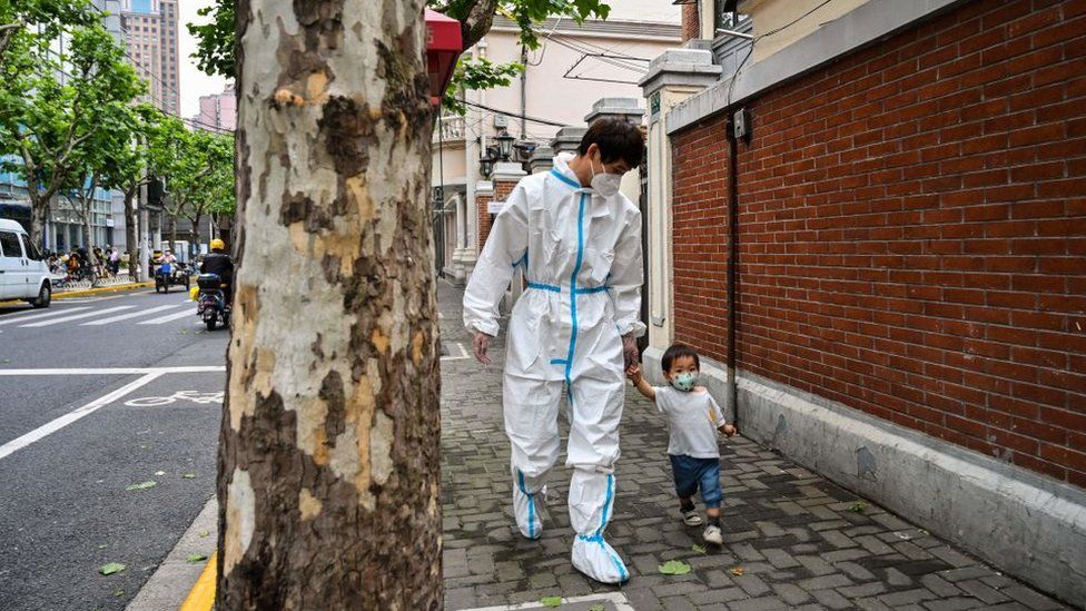 A worker wearing personal protective equipment (PPE) walks with a child on a street during a Covid-19 coronavirus lockdown in the Jing'an district of Shanghai on May 30, 2022.
